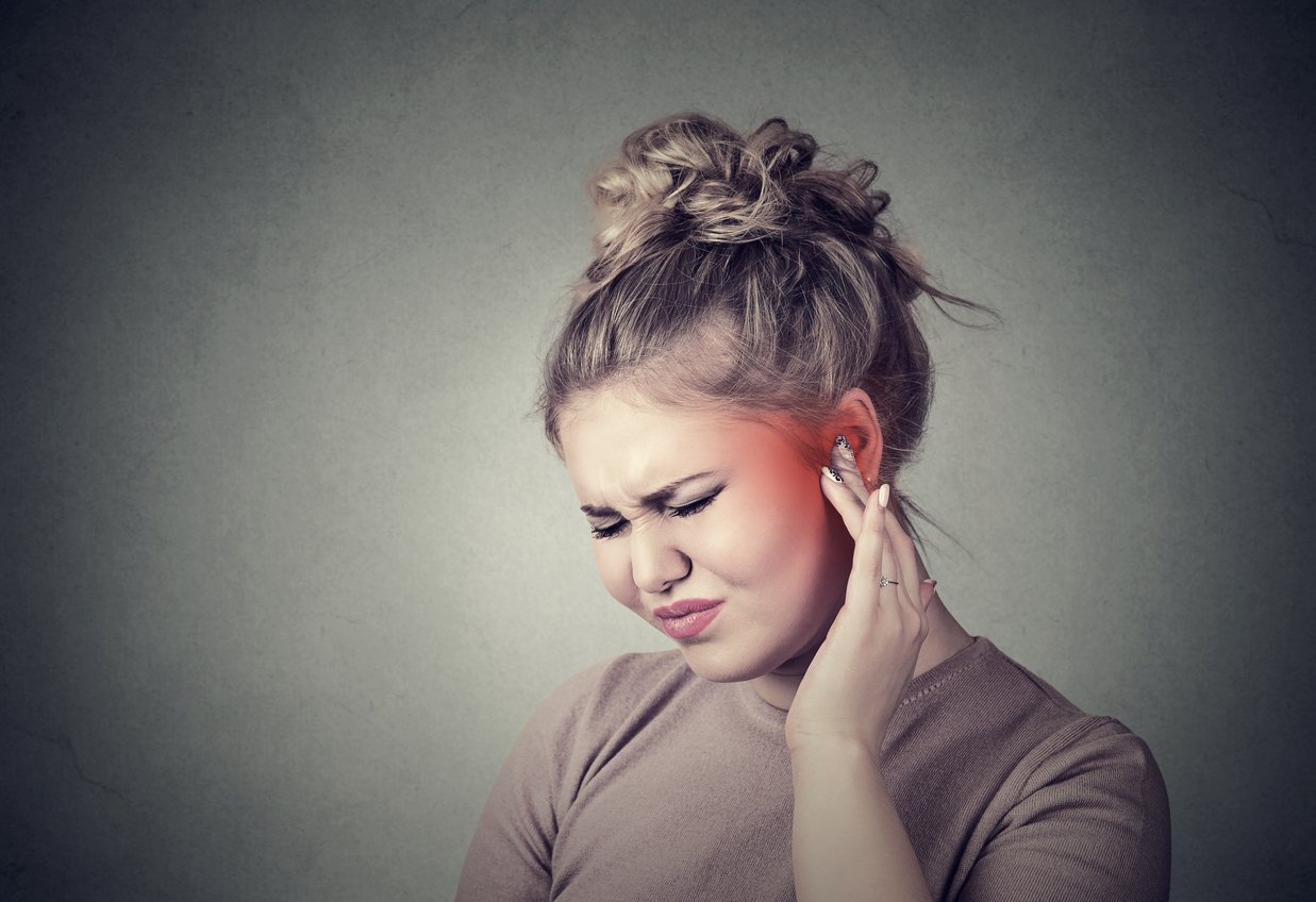 Tinnitus. Closeup up side profile sick female having ear pain touching her painful head colored in red isolated on gray background